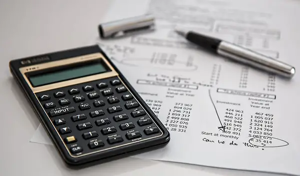 A calculator, a piece of paper, and a pen on a white surface