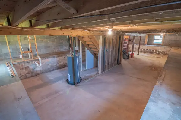 A water heater in an empty basement. Placing the water heater in line with the stairwell can be an excellent position to hide your water heater during renovations.